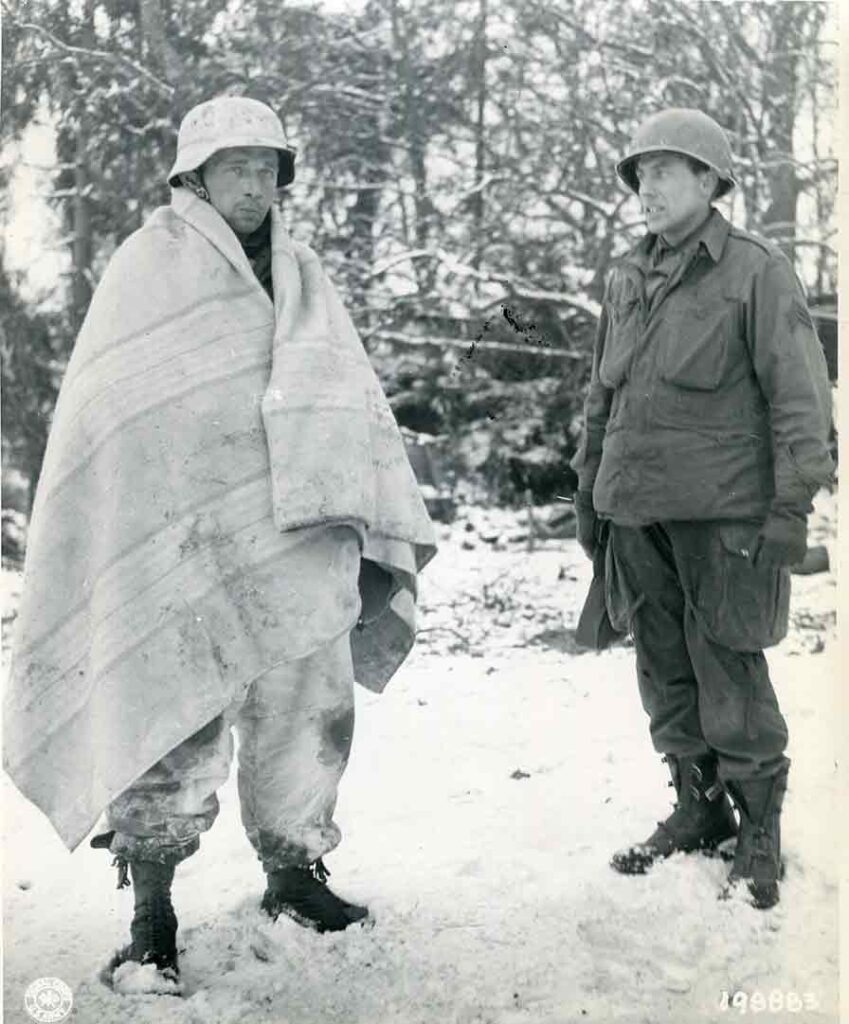 Sergeant Charles J. Ten Barges of the 325th GIR guards a captured SS soldier who is using a light-colored blanket as winter camouflage, 7 January 1945. (National Archives) 