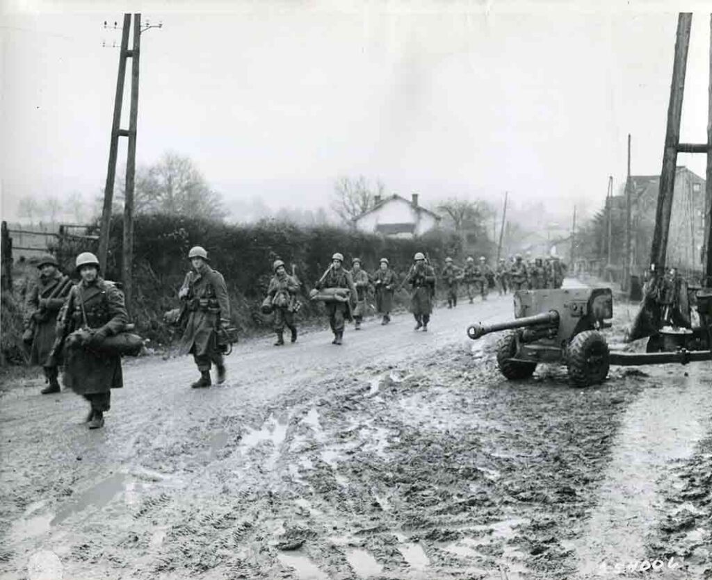 Paratroopers of 504th PIR pass by an abandoned 57mm antitank gun in the streets of Cheneux, 22 December 1944. (National Archives) 