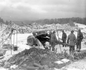 Snow falls on the camouflage net of a 155mm M1 Howitzer of the 254th Field Artillery Battalion, firing in support of the 82d Airborne Division at Werbomont, Belgium, 22 January 1945. (National Archives)