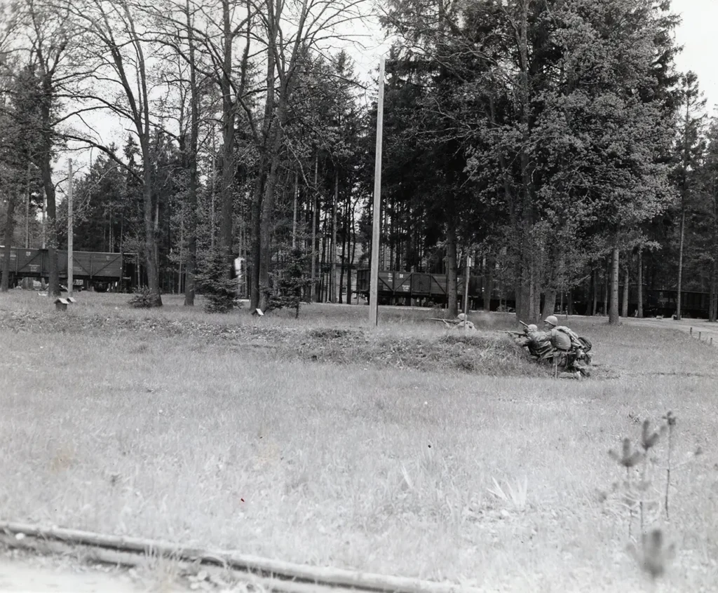 Soldiers from 3d Battalion, 157th Infantry Regiment, 45th Infantry Division, engage fleeing SS camp guards during the liberation of Dachau concentration camp, 29 April 1945. In the background are the infamous train cars containing many dead prisoners. (National Archives) 
